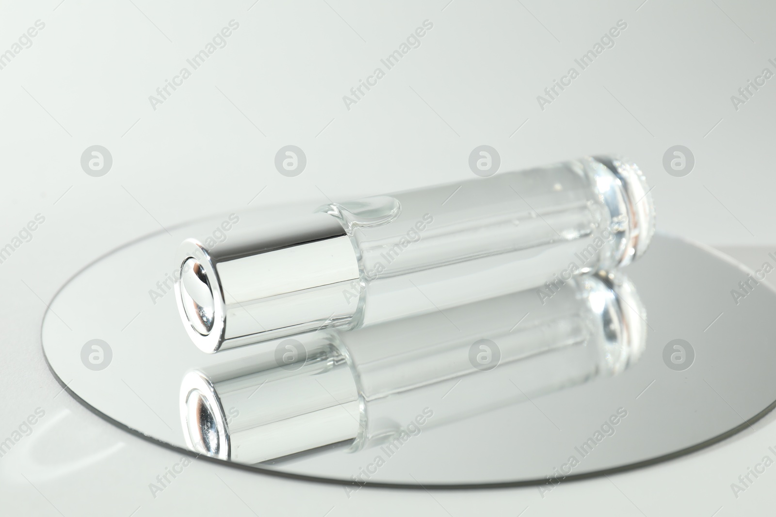 Photo of Bottle of serum and mirror on light background, closeup