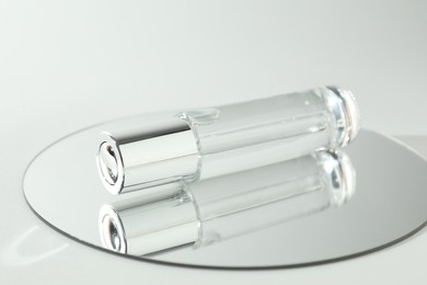 Bottle of serum and mirror on light background, closeup