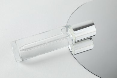 Photo of Bottle of serum and mirror on light background, closeup