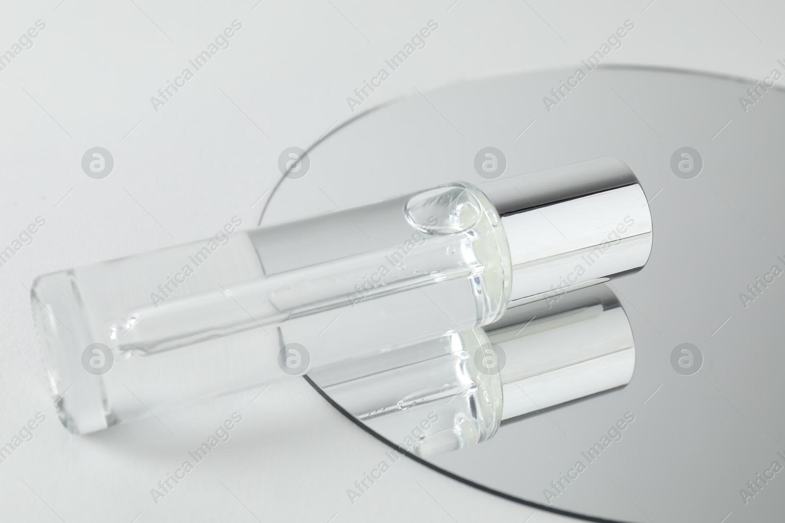 Photo of Bottle of serum and mirror on light background, closeup