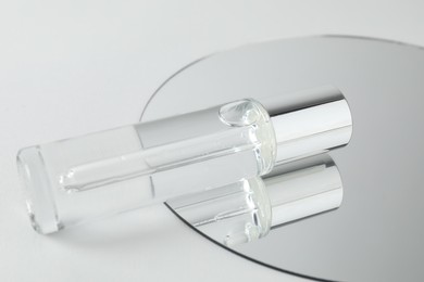 Photo of Bottle of serum and mirror on light background, closeup