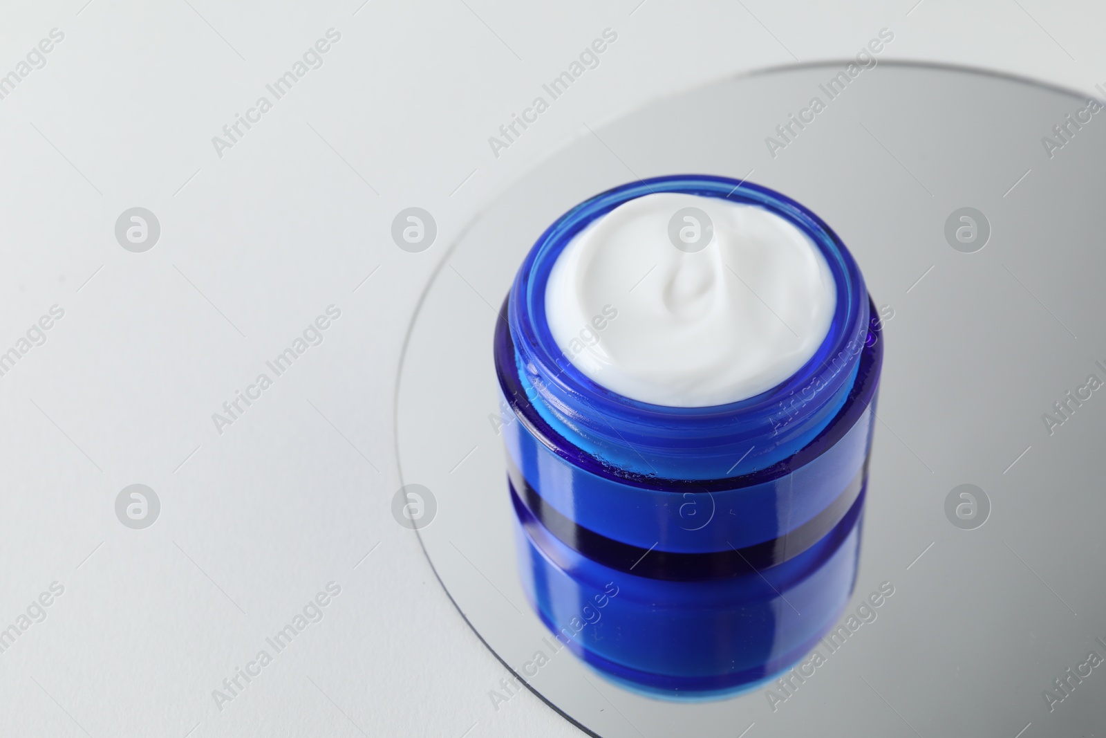 Photo of Jar of cream and mirror on light background, closeup. Space for text