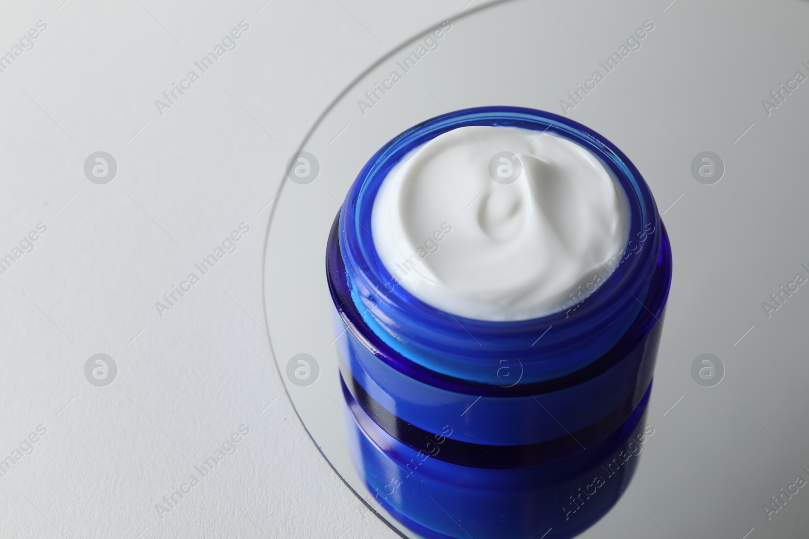 Photo of Jar of cream and mirror on light background, closeup. Space for text