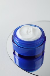 Photo of Jar of cream and mirror on light background, closeup