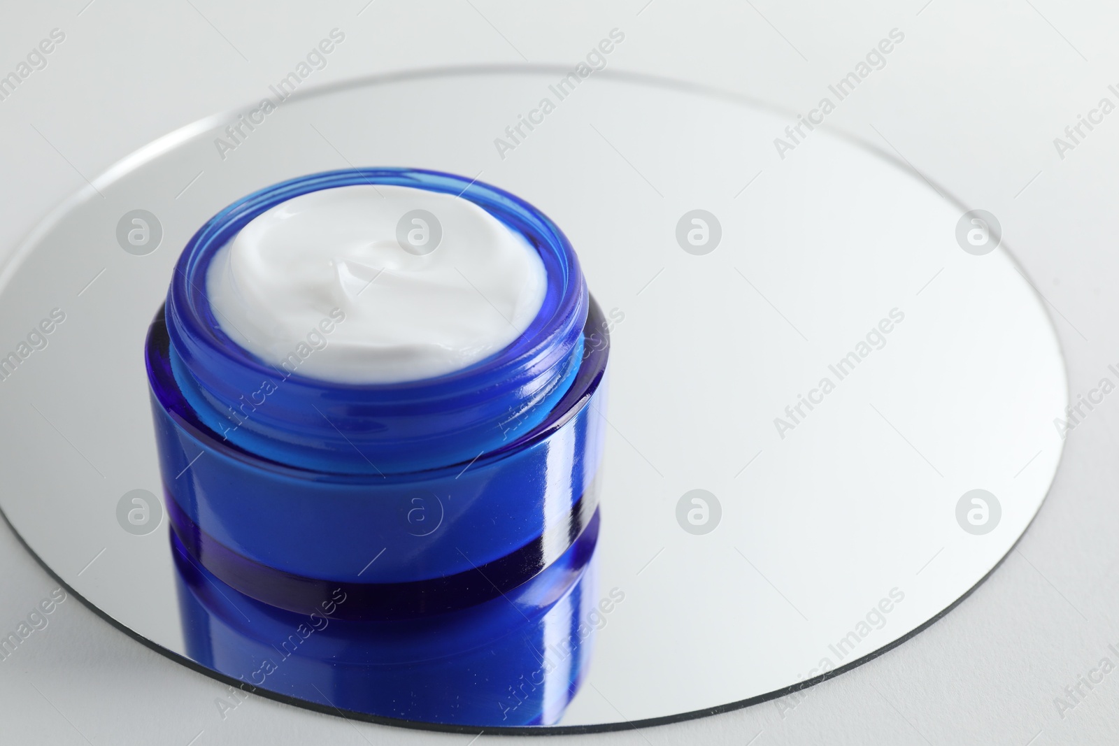 Photo of Jar of cream and mirror on light background, closeup. Space for text