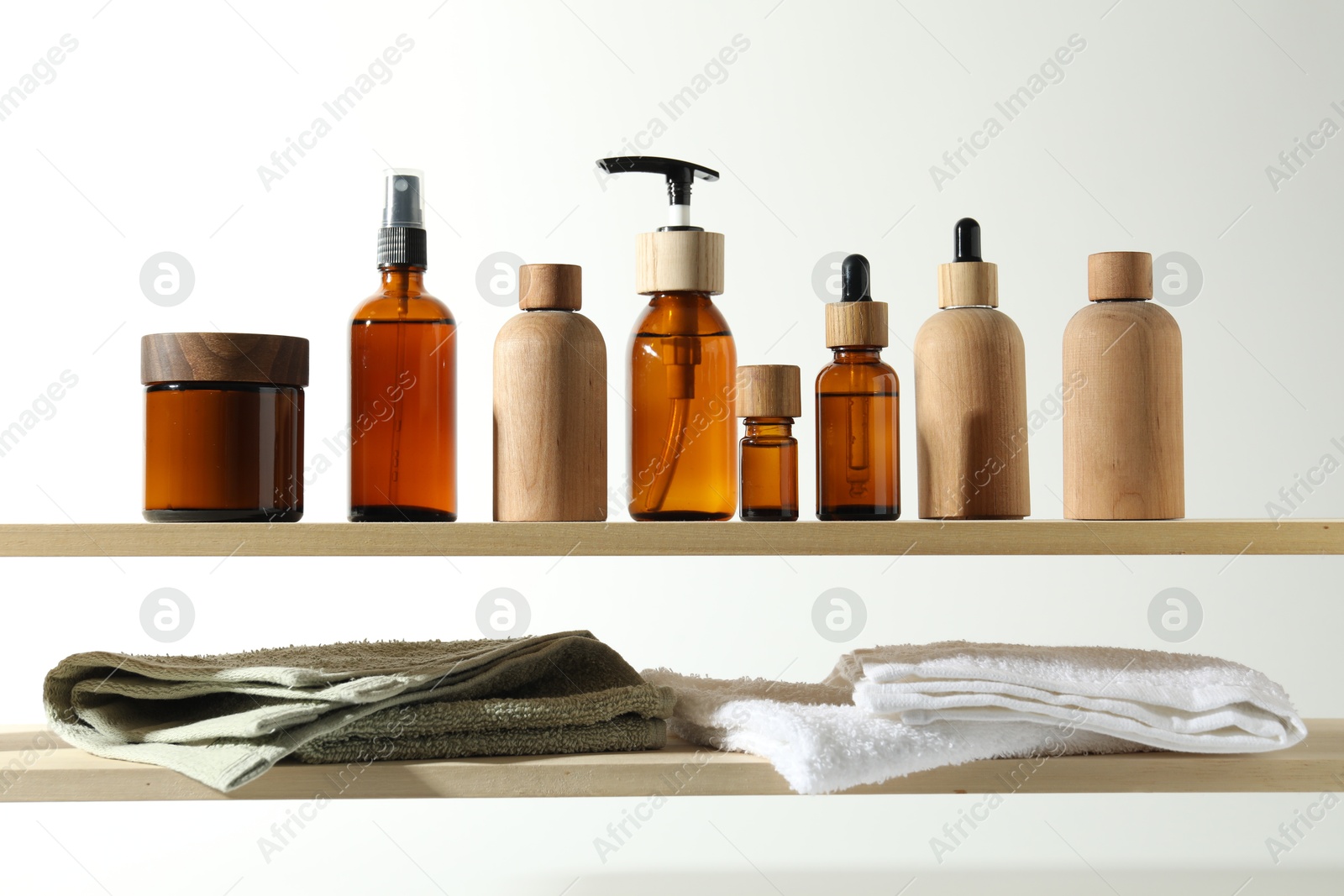 Photo of Different cosmetic products and towels on wooden shelves against white background