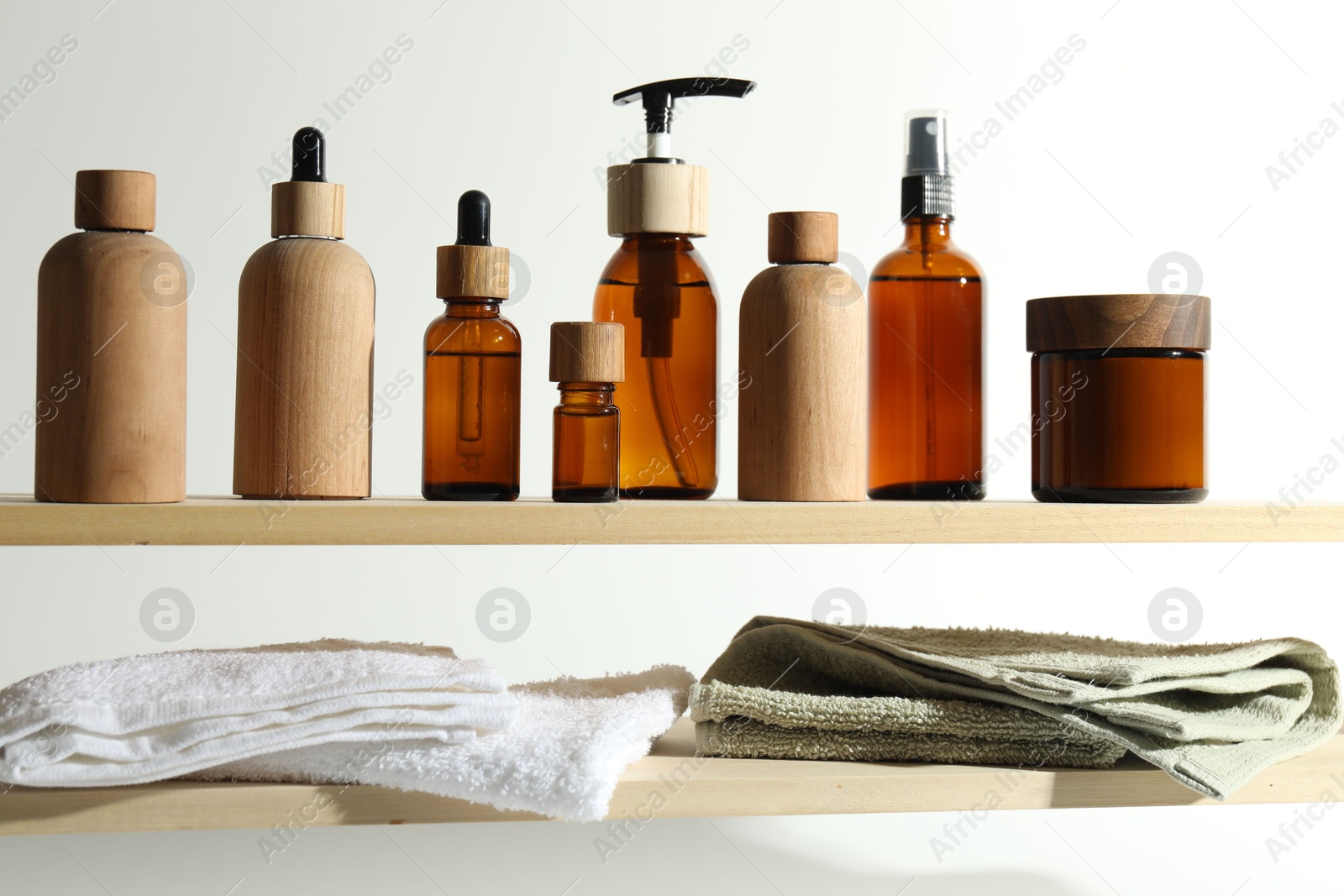 Photo of Different cosmetic products and towels on wooden shelves against white background