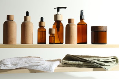 Different cosmetic products and towels on wooden shelves against white background