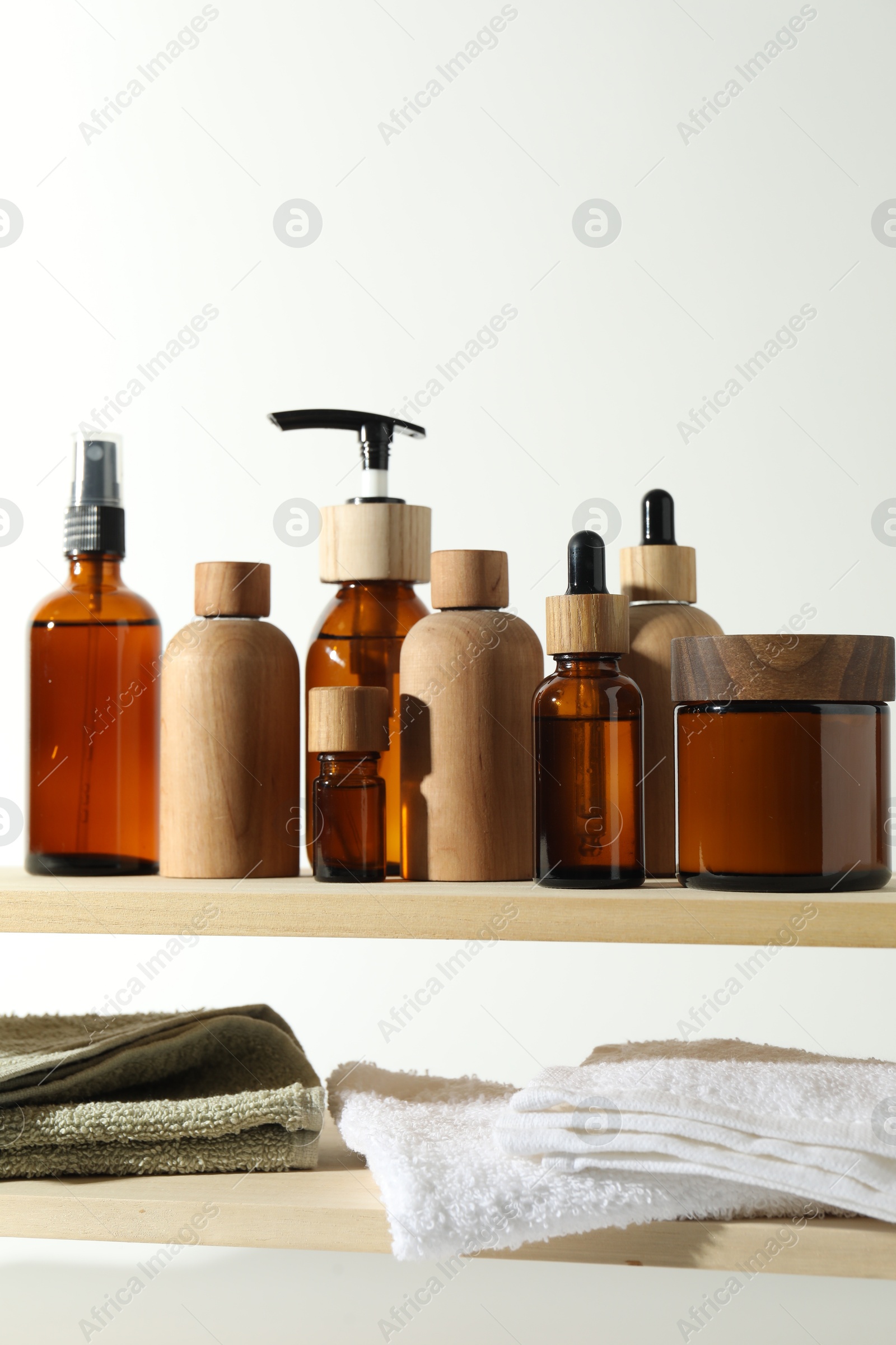 Photo of Different cosmetic products and towels on wooden shelves against white background, space for text