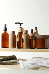 Photo of Different cosmetic products and towels on wooden shelves against white background, space for text