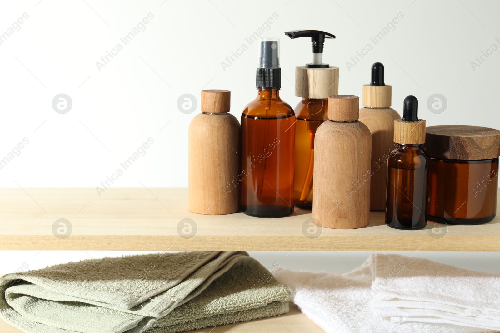 Photo of Different cosmetic products and towels on wooden shelves against white background