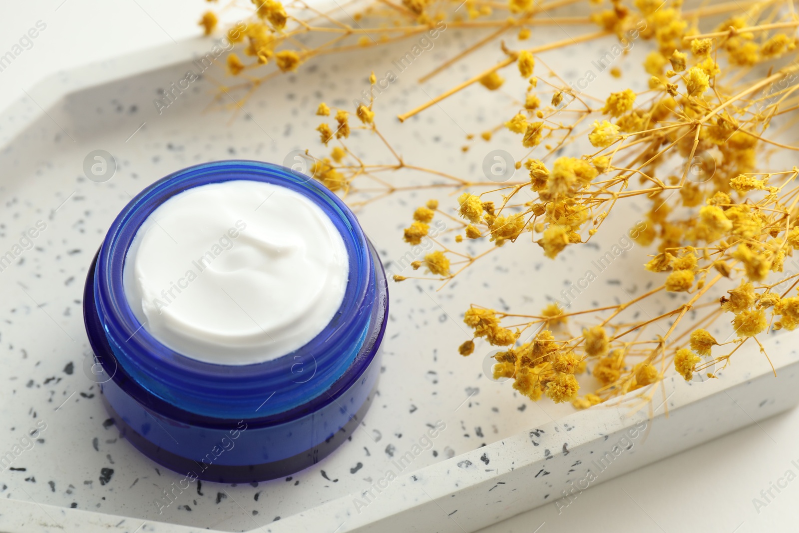 Photo of Jar of cream and yellow gypsophila flowers on table, closeup