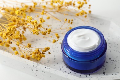 Jar of cream and yellow gypsophila flowers on table, closeup