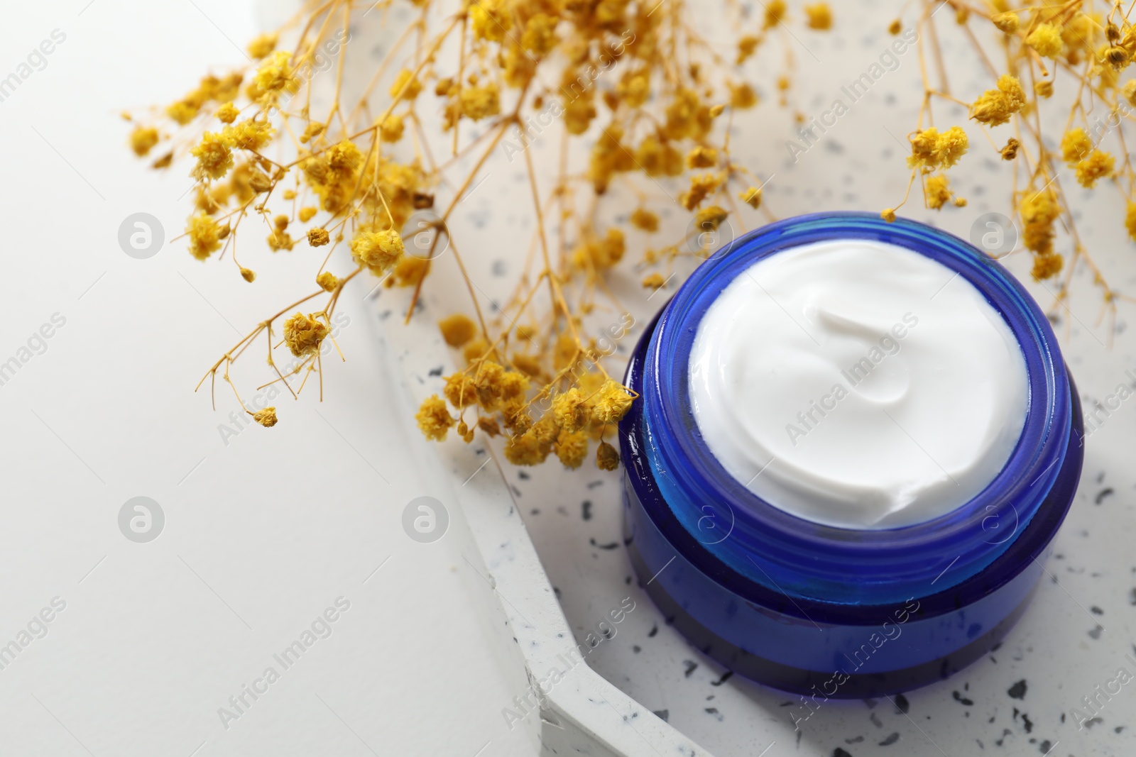 Photo of Jar of cream and yellow gypsophila flowers on white background, closeup. Space for text