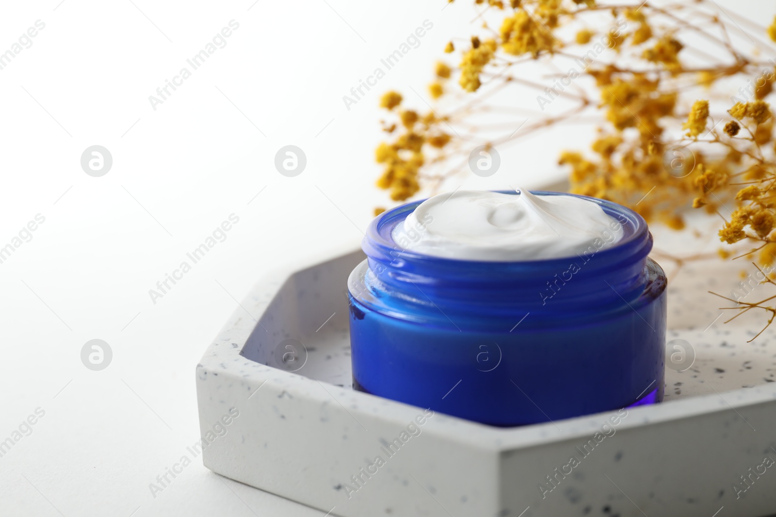 Photo of Jar of cream and yellow gypsophila flowers on white background, closeup. Space for text