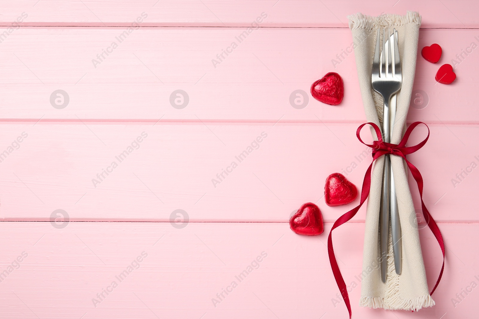 Photo of Romantic place setting for Valentine's day. Cutlery, napkin and decorative hearts on pink wooden table, flat lay. Space for text