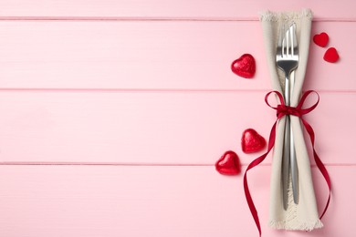 Photo of Romantic place setting for Valentine's day. Cutlery, napkin and decorative hearts on pink wooden table, flat lay. Space for text