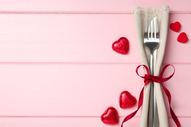 Photo of Romantic place setting for Valentine's day. Cutlery, napkin and decorative hearts on pink wooden table, flat lay. Space for text