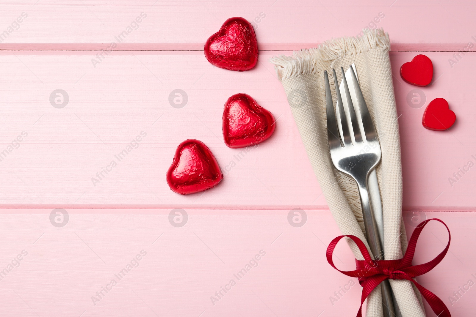 Photo of Romantic place setting for Valentine's day. Cutlery, napkin and decorative hearts on pink wooden table, flat lay. Space for text