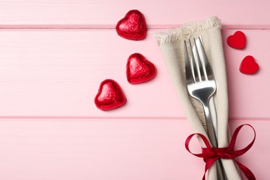 Photo of Romantic place setting for Valentine's day. Cutlery, napkin and decorative hearts on pink wooden table, flat lay. Space for text