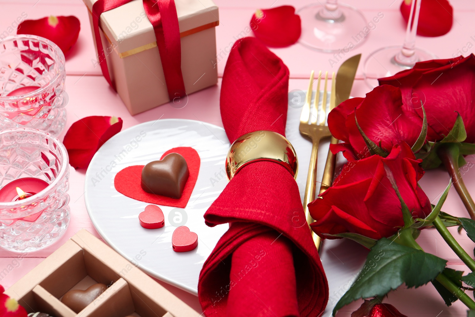 Photo of Romantic place setting for Valentine's day. Plate, cutlery, napkin and roses on pink table, closeup