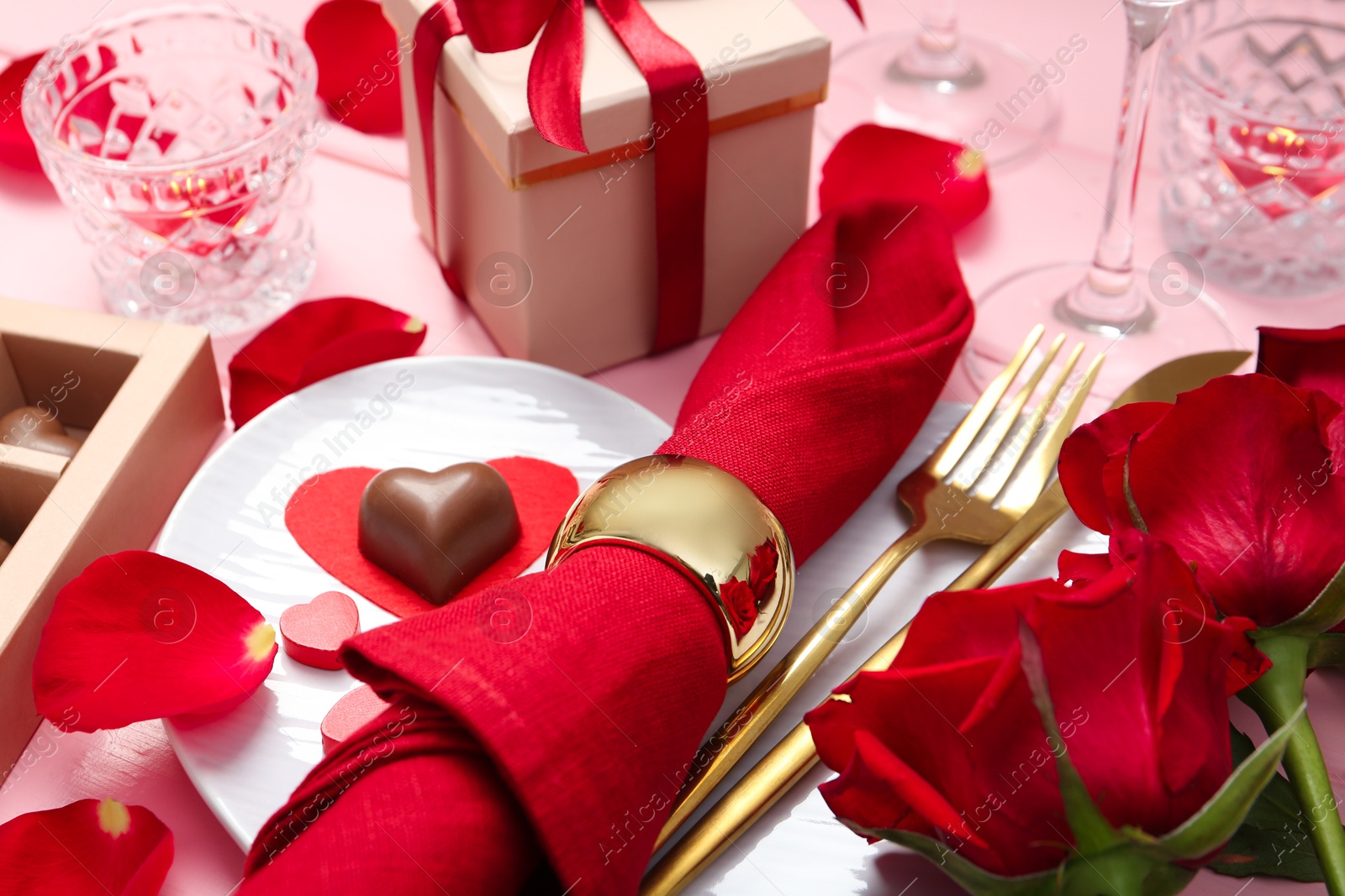 Photo of Romantic place setting for Valentine's day. Plate, cutlery, napkin and roses on pink table, closeup