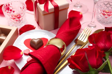 Photo of Romantic place setting for Valentine's day. Plate, cutlery, napkin and roses on pink table, closeup