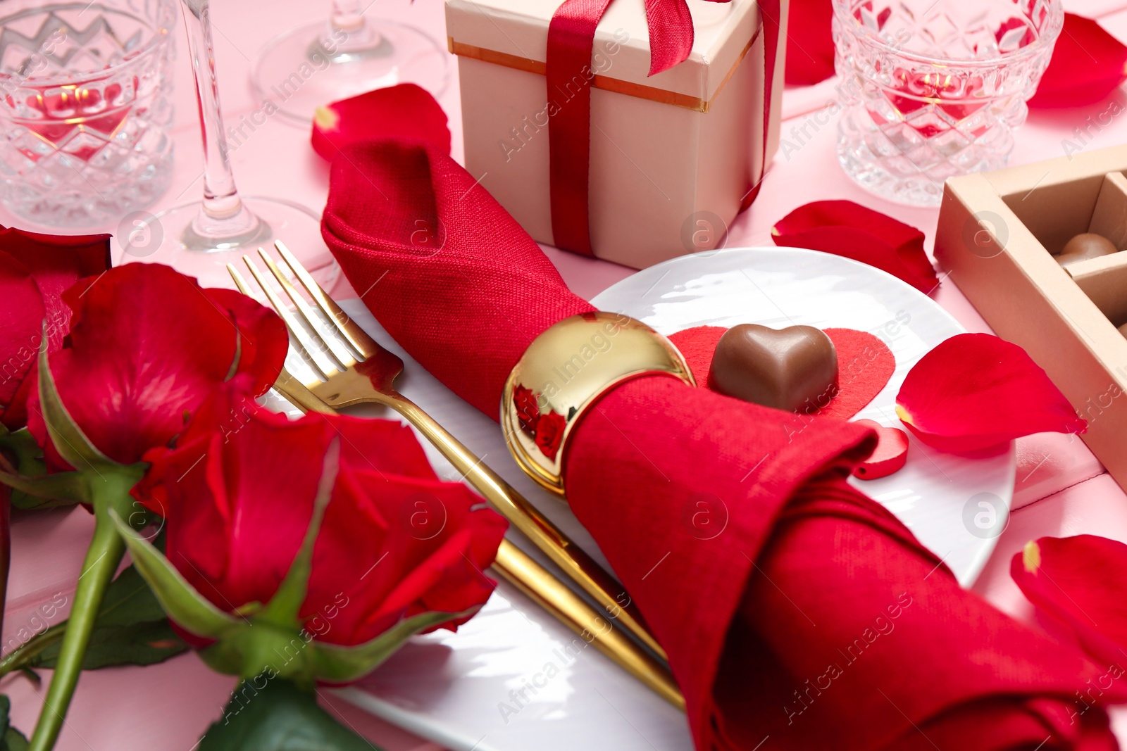 Photo of Romantic place setting for Valentine's day. Plate, cutlery, napkin and roses on pink table, closeup