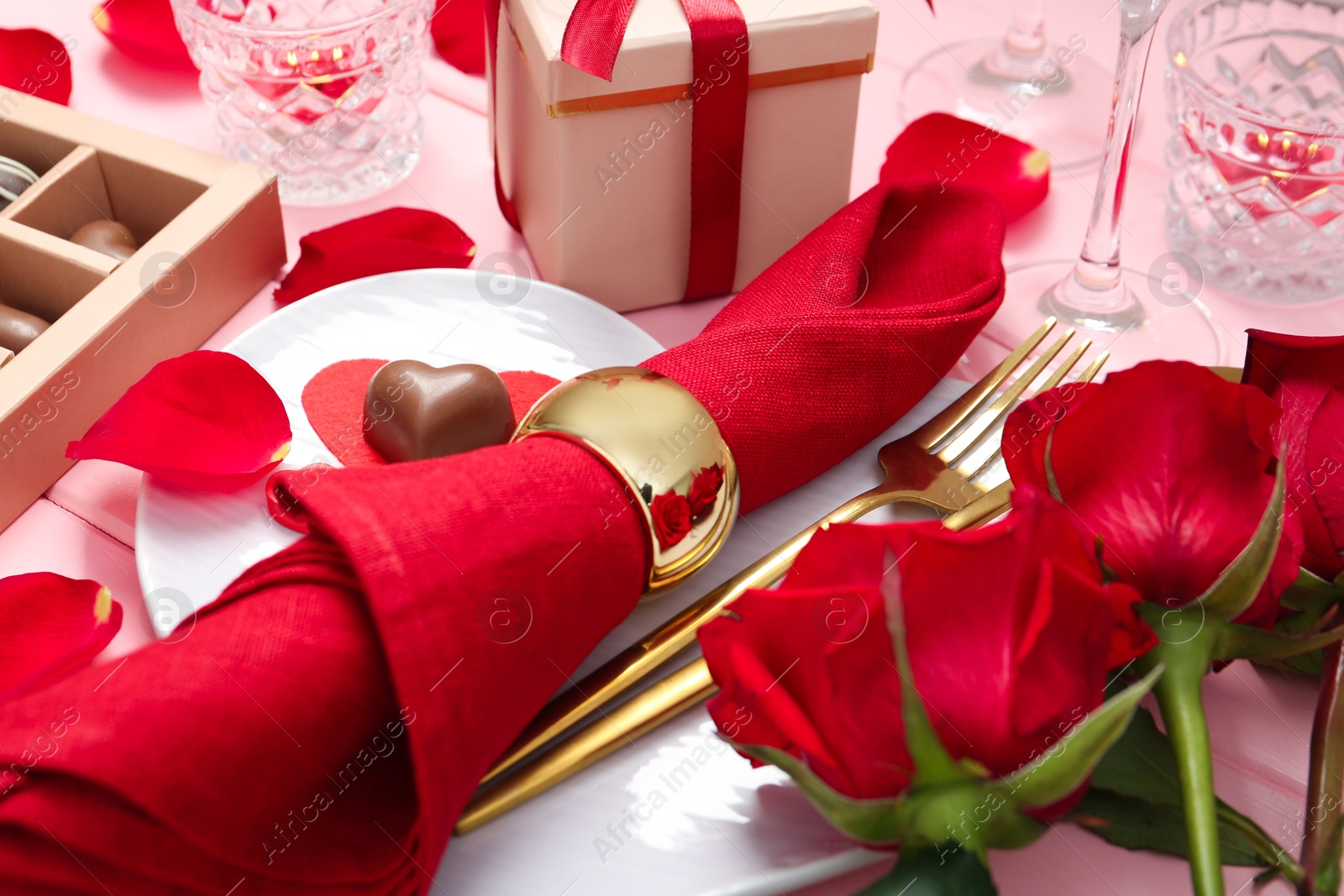 Photo of Romantic place setting for Valentine's day. Plate, cutlery, napkin and roses on pink table, closeup