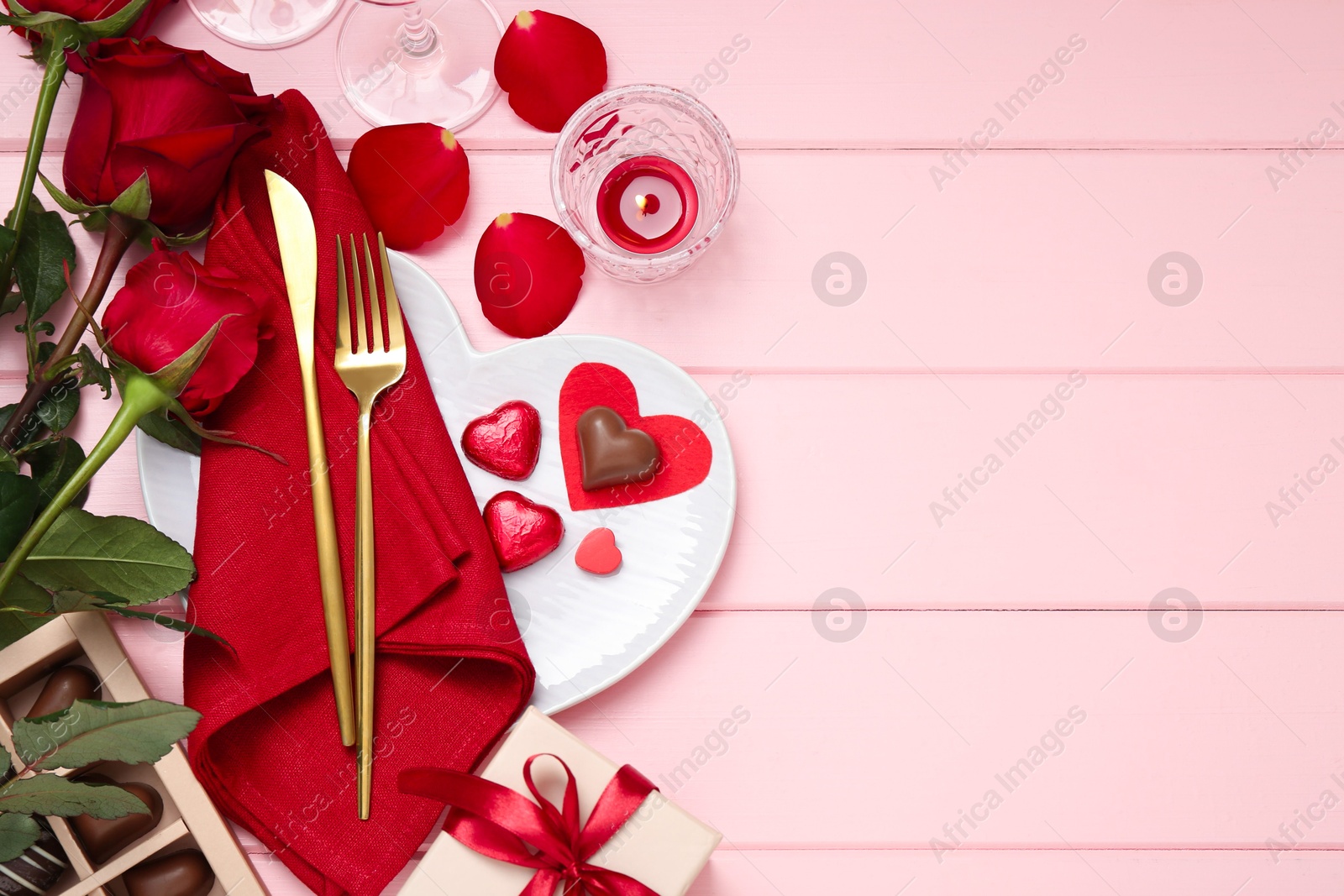 Photo of Romantic place setting for Valentine's day. Cutlery, napkin, plate, roses and decorative hearts on pink wooden table, flat lay. Space for text