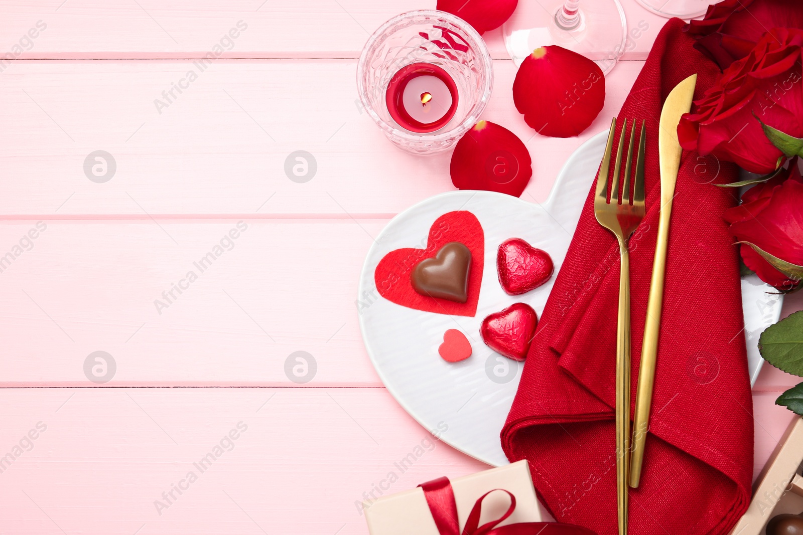 Photo of Romantic place setting for Valentine's day. Cutlery, napkin, plate, roses and decorative hearts on pink wooden table, flat lay. Space for text