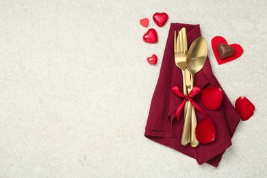 Photo of Romantic place setting for Valentine's day. Cutlery, napkin, candy, petals and decorative hearts on light textured table, flat lay. Space for text