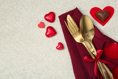 Photo of Romantic place setting for Valentine's day. Cutlery, napkin, candy, petals and decorative hearts on light textured table, flat lay. Space for text