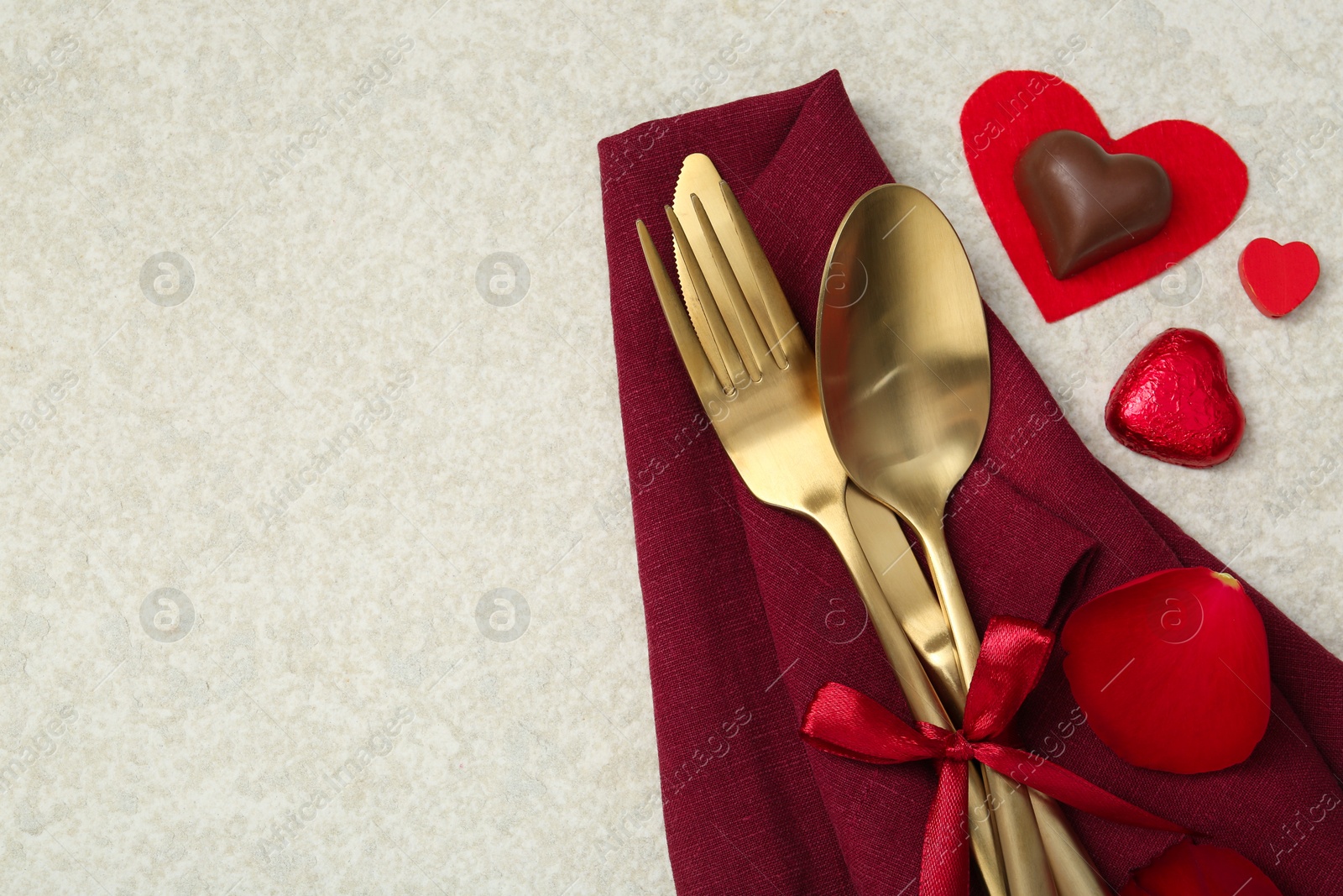 Photo of Romantic place setting for Valentine's day. Cutlery, napkin, candy, petals and decorative hearts on light textured table, flat lay. Space for text