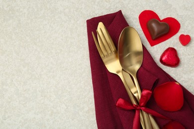 Photo of Romantic place setting for Valentine's day. Cutlery, napkin, candy, petals and decorative hearts on light textured table, flat lay. Space for text