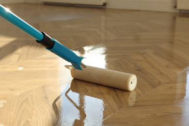 Photo of Polishing parquet with roller and varnish indoors, closeup