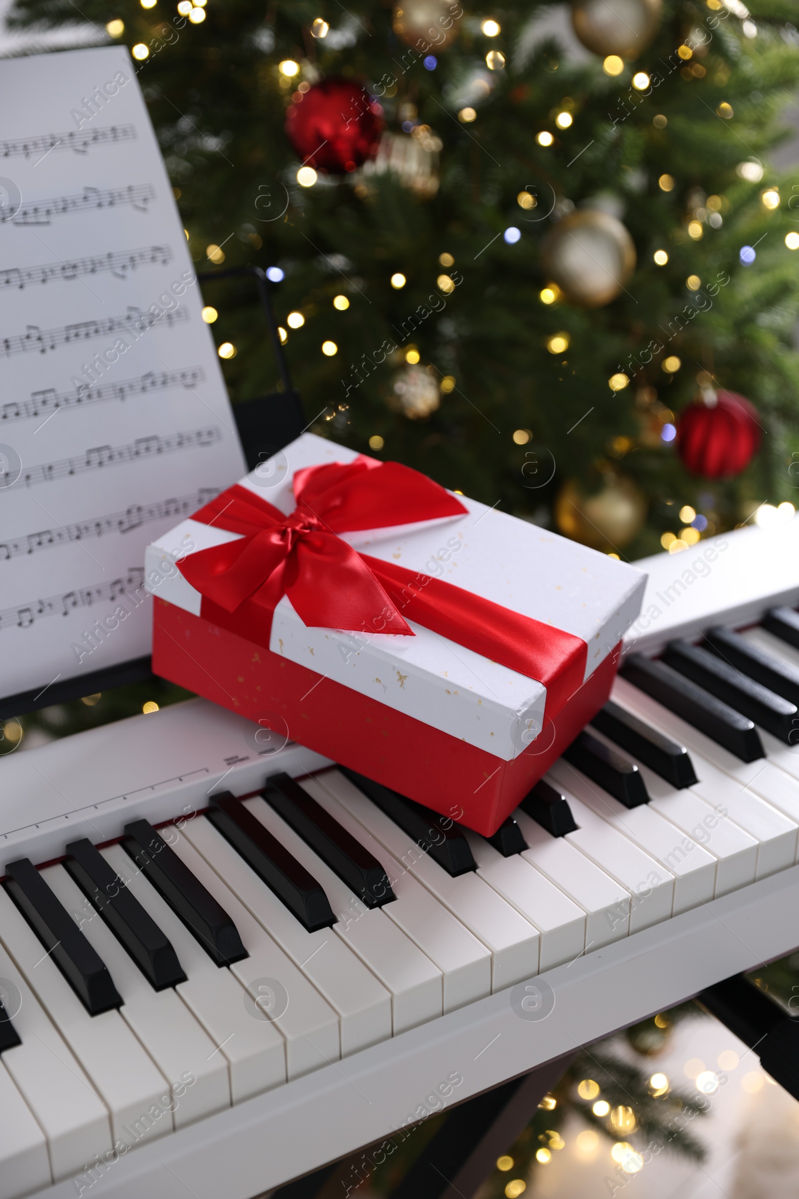 Synthesizer with music sheet and gift box near Christmas tree indoors, closeup Photo of Synthesizer with music sheet and gift box near Christmas tree indoors, closeup