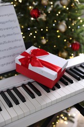 Photo of Synthesizer with music sheet and gift box near Christmas tree indoors, closeup