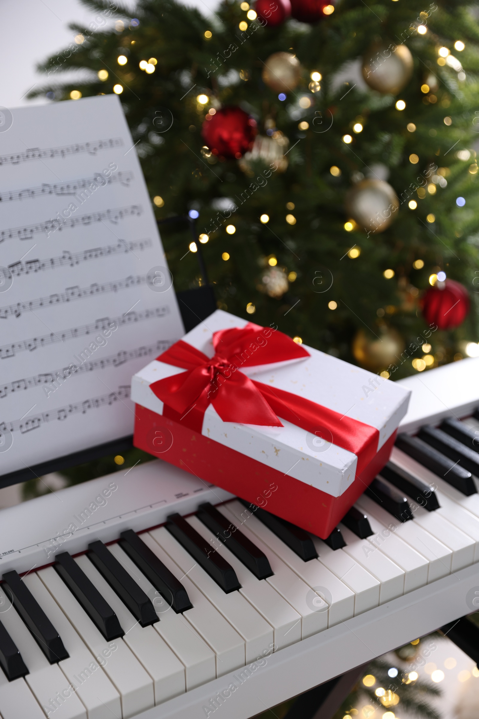 Photo of Synthesizer with music sheet and gift box near Christmas tree indoors, closeup