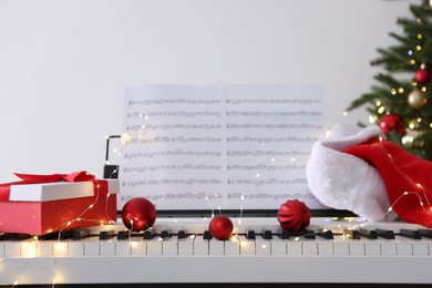 Photo of Synthesizer with music sheets and festive decor near Christmas tree indoors, closeup