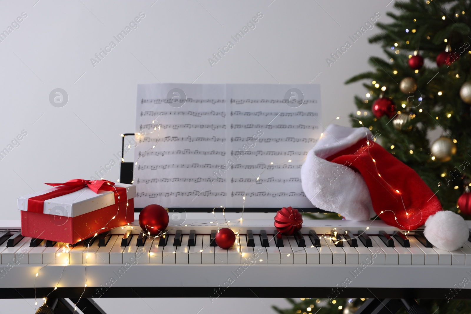 Synthesizer with music sheets and festive decor near Christmas tree indoors Photo of Synthesizer with music sheets and festive decor near Christmas tree indoors