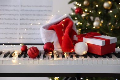 Photo of Synthesizer with music sheets and festive decor near Christmas tree indoors, closeup