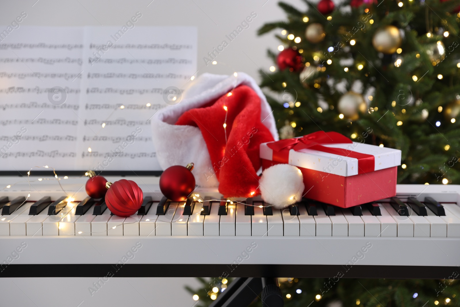 Synthesizer with music sheets and festive decor near Christmas tree indoors, closeup Photo of Synthesizer with music sheets and festive decor near Christmas tree indoors, closeup