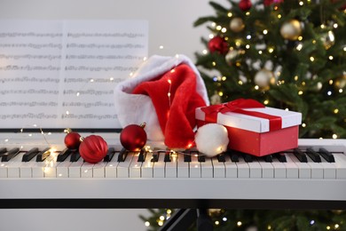 Photo of Synthesizer with music sheets and festive decor near Christmas tree indoors, closeup