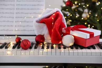 Synthesizer with music sheets and festive decor near Christmas tree indoors, closeup