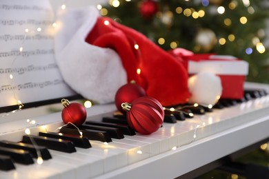 Photo of Synthesizer with music sheets and Christmas decor against blurred festive lights, closeup