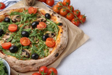 Photo of Tasty pizza with cherry tomatoes, black olives, mushrooms and arugula on light grey table, closeup. Space for text