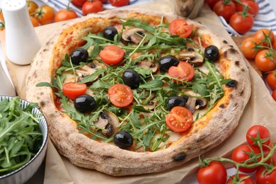 Photo of Tasty pizza with cherry tomatoes, black olives, mushrooms and arugula on table, closeup