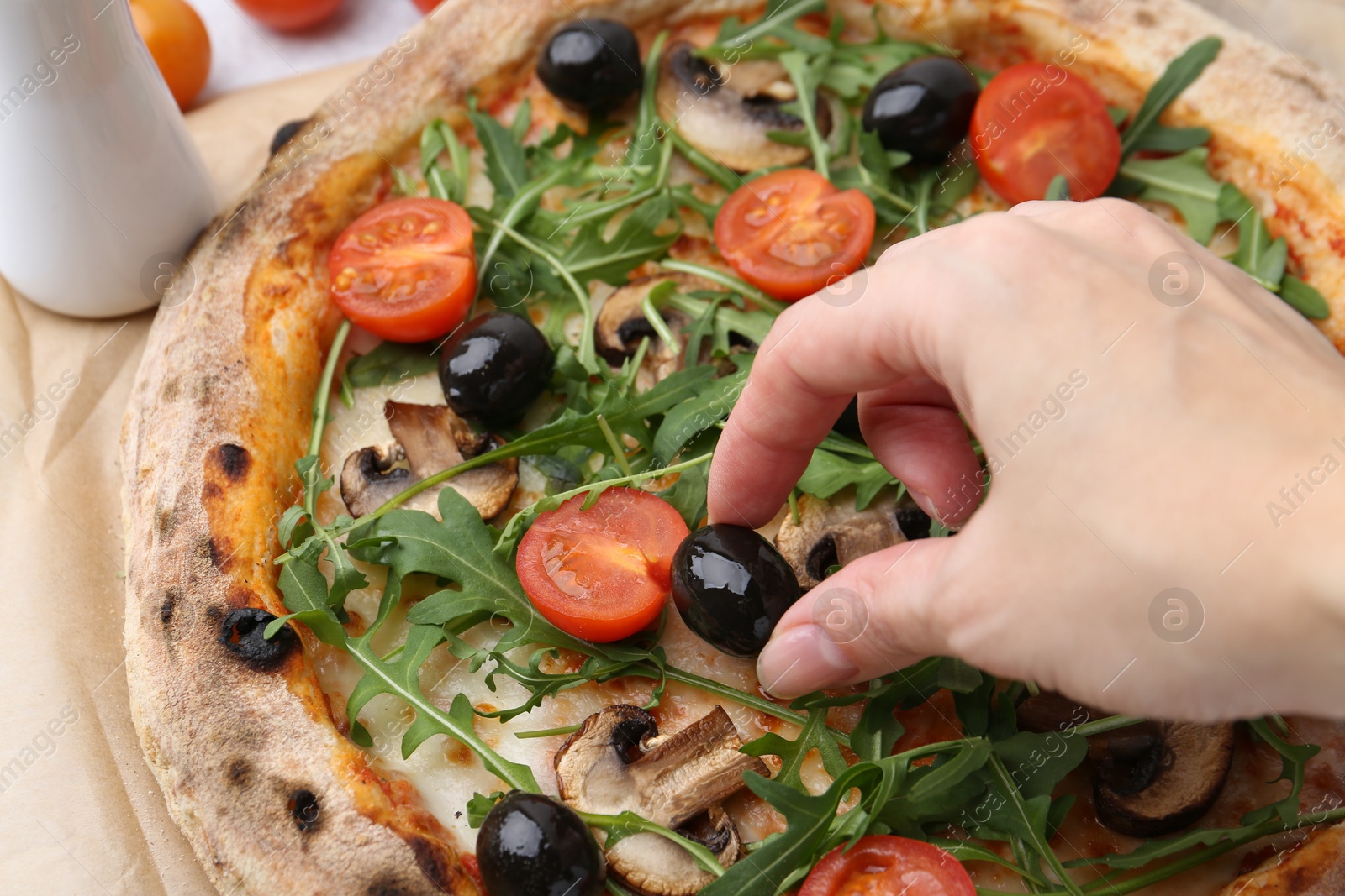 Photo of Woman putting black olive onto tasty pizza at table, closeup