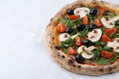 Photo of Tasty pizza with cherry tomatoes, black olives, mushrooms and arugula on white tiled table, closeup. Space for text